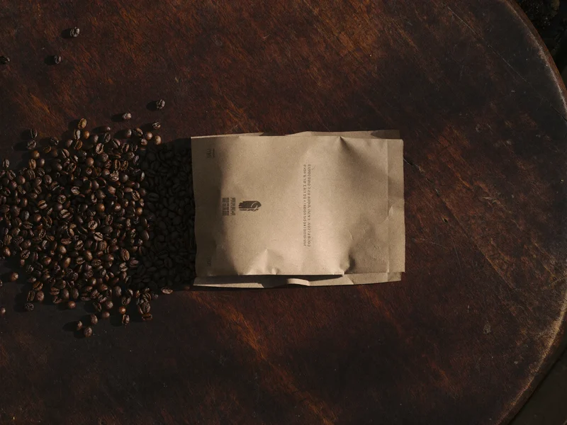 Sacchetto kraft senza marchio con chicchi di caffè tostato su tavolo scuro