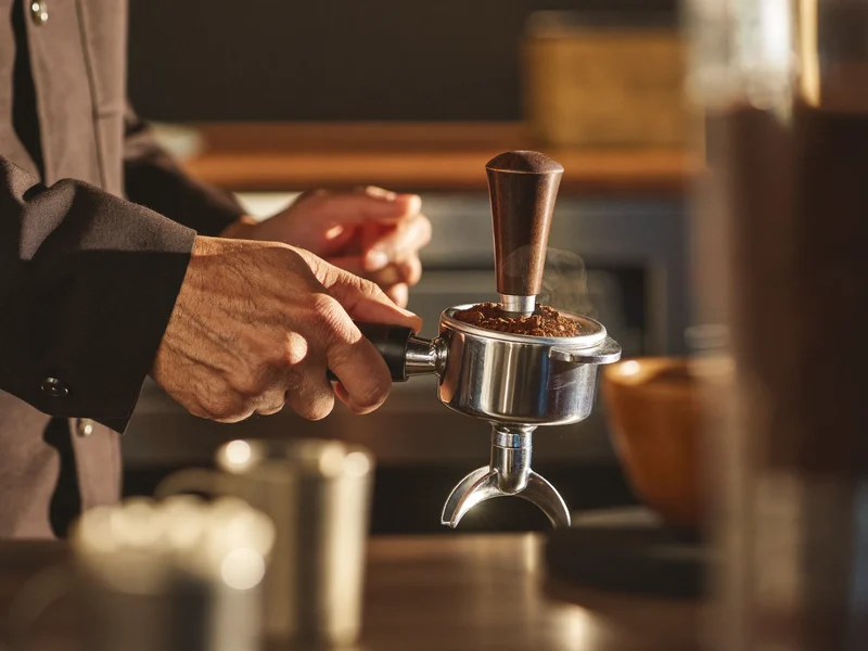 Barista che pressa il caffè macinato nel portafiltro al bancone espresso