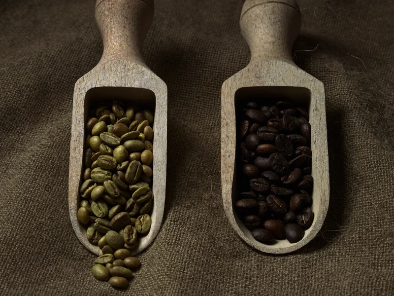 Chicchi di caffè verdi e tostati in due cucchiai di legno su tela