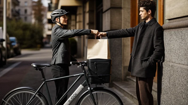 Corriere in bicicletta consegna un sacchetto di caffè all'ingresso di un palazzo